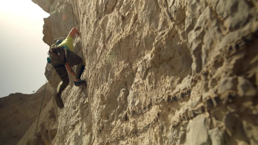 A person wearing a helmet climbs the a rough cliff at daytime