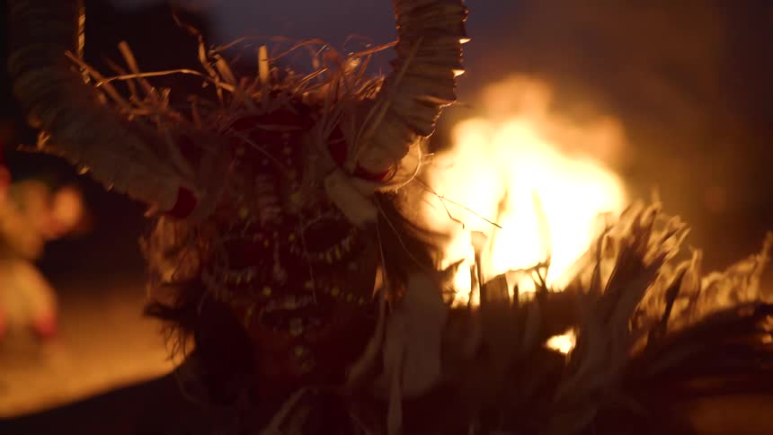 A group of people dressed in costumes and masked dancing on the beach at night around a bonfire