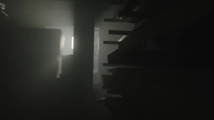 Light shines through the windows of a cluttered smoke filled room with a stack of boxes and a shelf