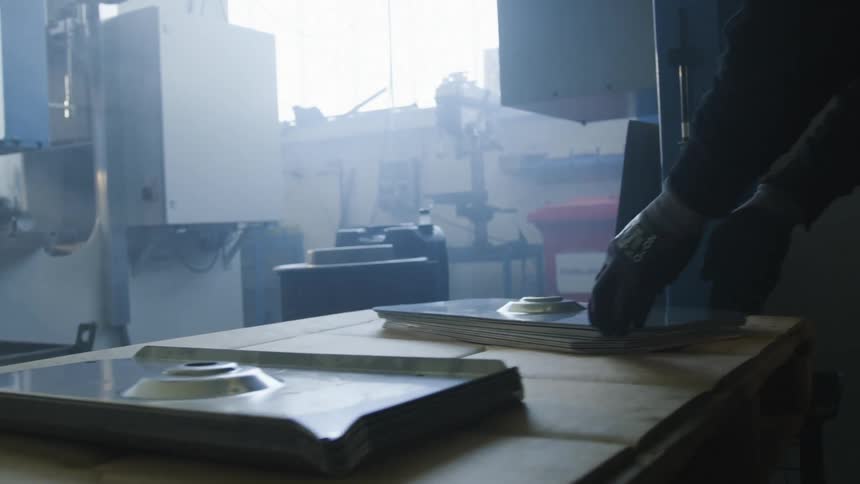 A man is standing near a table moving metal parts and putting them into a machine