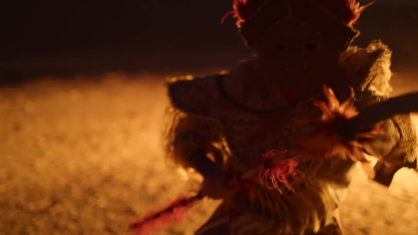 Silhouette of a dancer wearing ceremonial clothes dancing in front of a bonfire