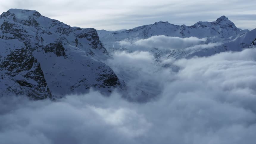 Aerial View: Clouds Enveloping Snowy Mountain Range in Daytime