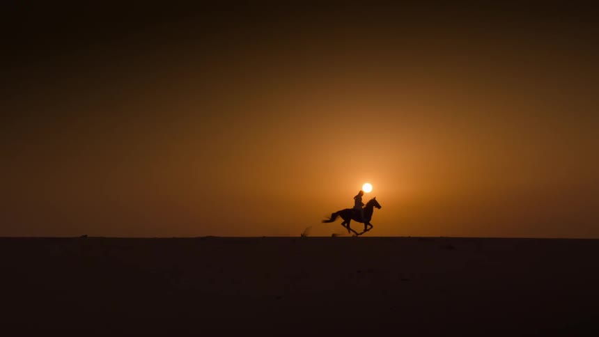 A silhouette of a man riding a horse through the desert with the sun setting behind them