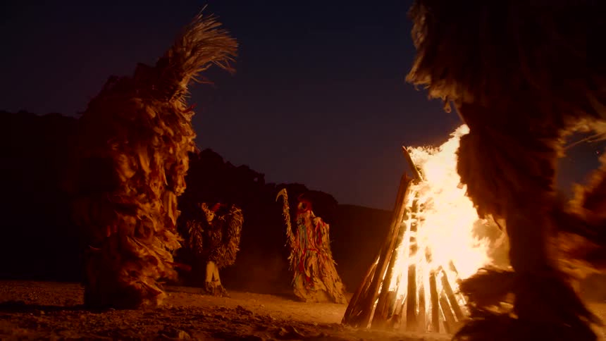 The view is of people dancing around the fire at night time