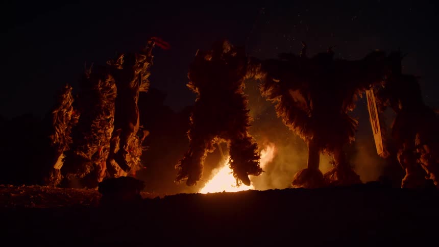 Silhouette of a group of dancers wearing ceremonial clothes in front of a bonfire at night