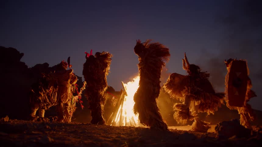 Silhouette of a group of dancers wearing ceremonial clothes in front of a bonfire at night