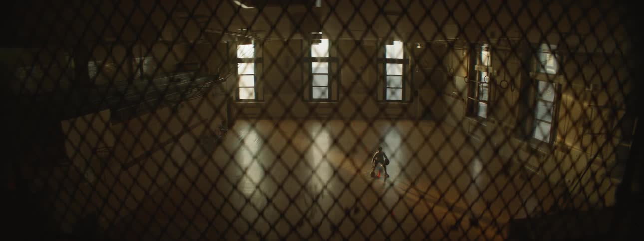 View through a fence looking down at a basketball player dribbling two balls