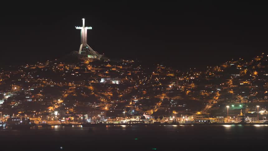 A large cross sits on a hill over a city