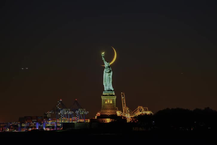 The moon goes down behind the statue of liberty