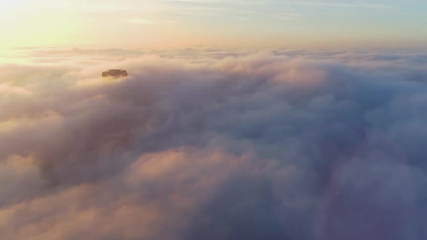 An aerial view above dense fluffy clouds with the sun and skies reflection on the clouds