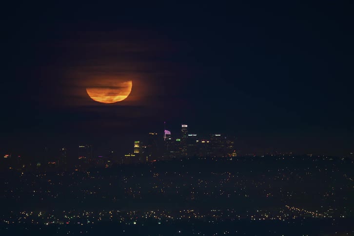 A large glowing moon above city skyscrapers at night