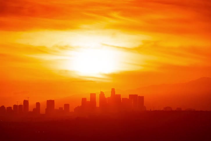 Silhouette of a metropolitan city with tall buildings and towers as a colorful sky moves overhead and the sun sets as city lights glow in the darkness