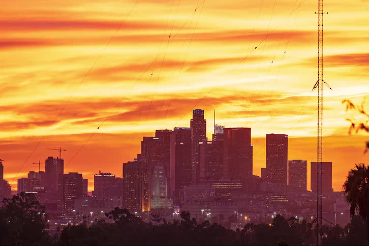 A time lapse of a city skyline with the sun setting and going yellow to red to orange at night as the building lights come on