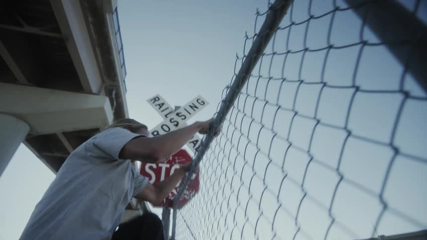 A group of young skateboarders jump over a chainlink fence