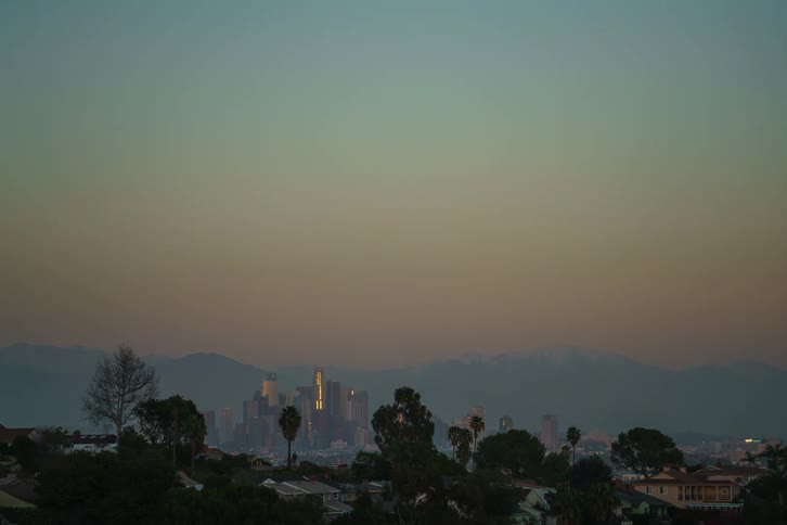 A time lapse view of a city skyline near mountains going from day to night as the moon rises in the sky