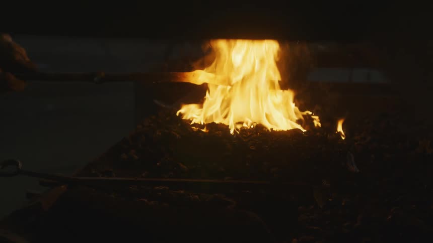 A contained fire burning in a pile as a person pulls a hot rod out of the fire