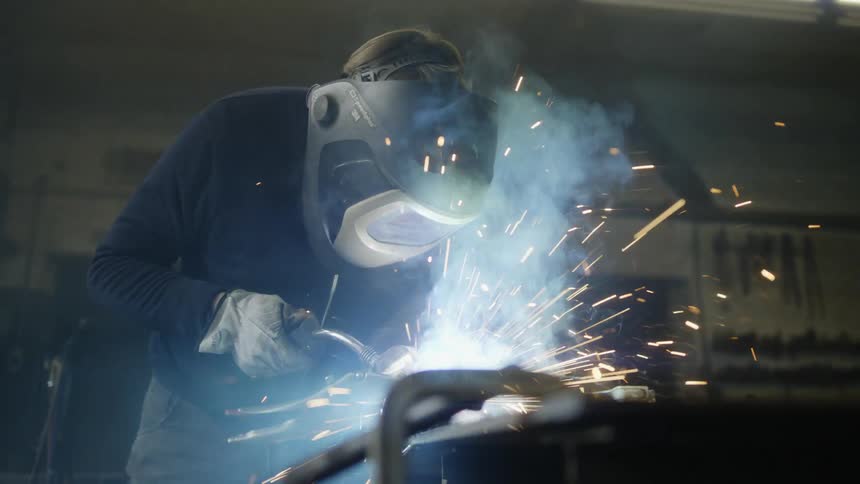 A welder wearing a mask is using a welding torch inside a garage