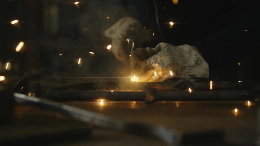 Man with dirty gloves and black jacket uses welding machine