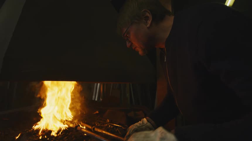 An up close of a man wearing gloves handling hot bars submerged in a fire in a controlled area