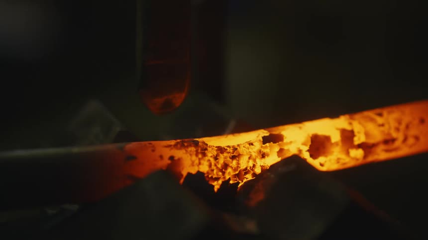 A close up of a tool being wielded to make a whole or divet in the hot pipe