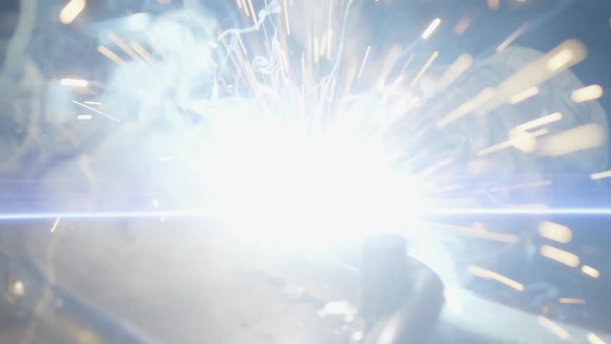 A close up of a person hands wearing gloves as they weld metal together creating bright sparks