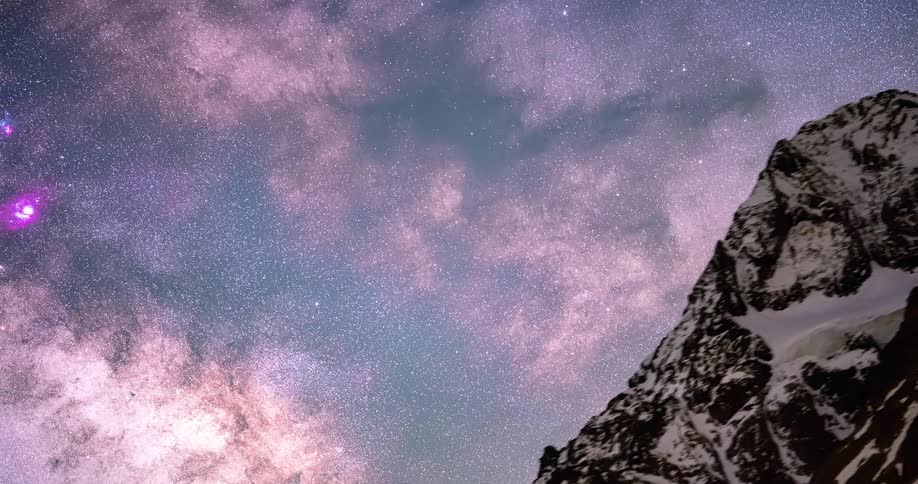 A starry night sky with snowy mountain peaks in front of it