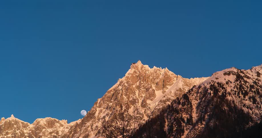 A time lapse of the peak of a mountain range with snow on the ridges as the moon comes up over the ridge
