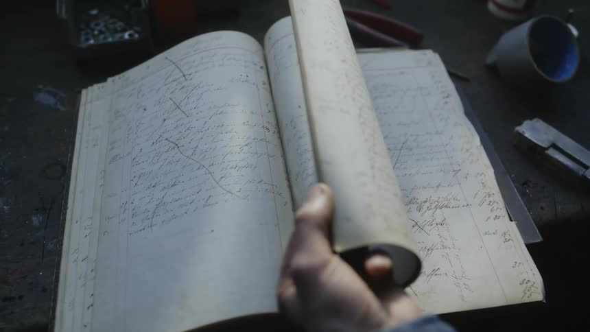 Man turns handwritten pages of notebook on workbench