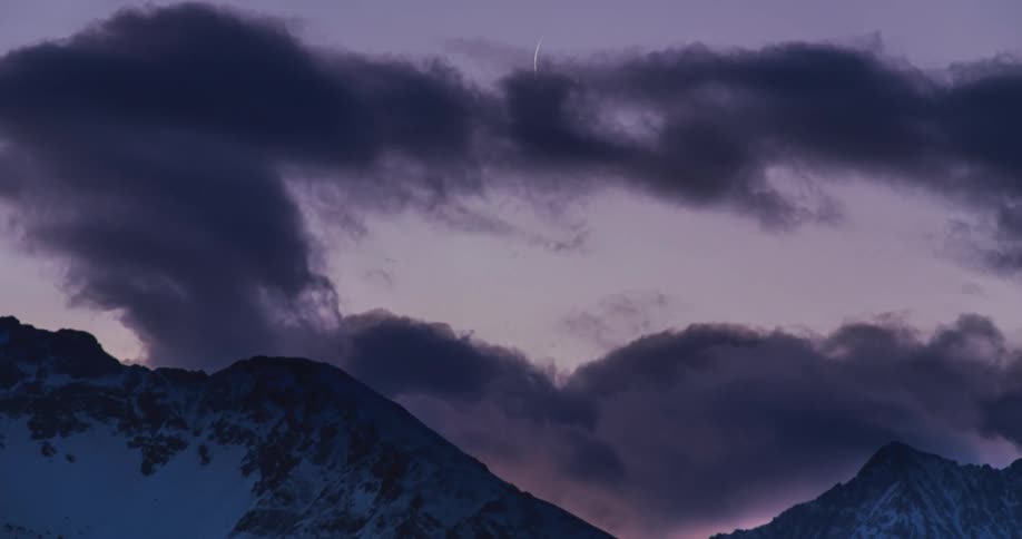 Time lapse of moon rising over the mountains behind the rolling clouds at evening