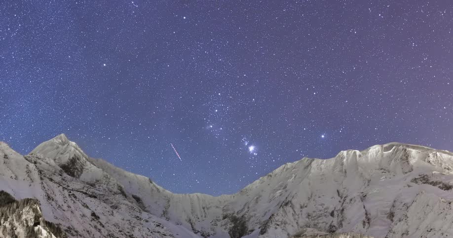 Stars move over mountains as shooting stars fly across the sky