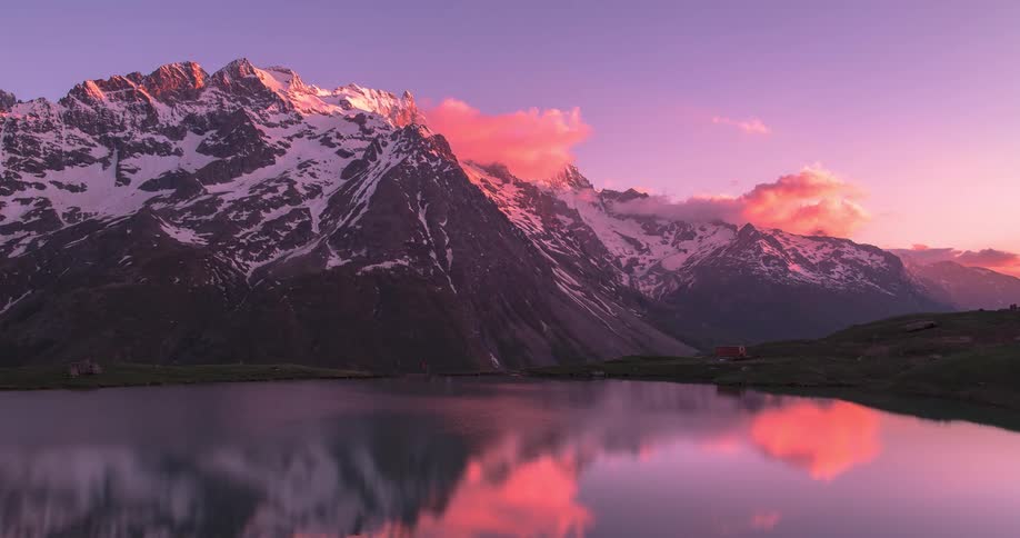 Homes sit on shore of lake reflecting snowy mountain and red clouds during sunset