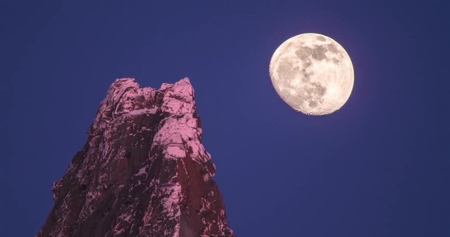 Time lapse footage of the moon rising over a mountain peak at night