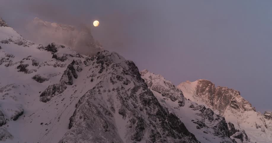Astronomical body moves over snow covered mountain as sky brightens