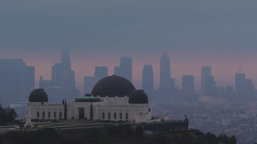 Aerial of the Griffith Observatory with skyscrapers from Los Angeles in the distance at sunset