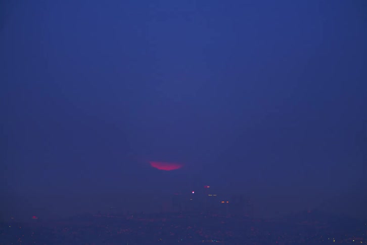 A foggy time lapse of the moon lowering over a city in the distance
