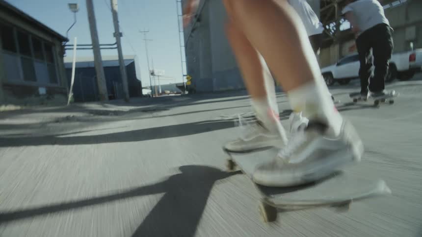 A group of three teenage boys ride skateboards eagerly across an urban industrial alley