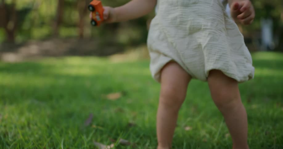 A toddler walking in the grass away from an adult sitting behind them