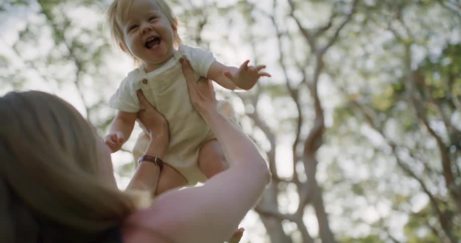 Mother with brown hair and black blouse holds toddler girl in the public park