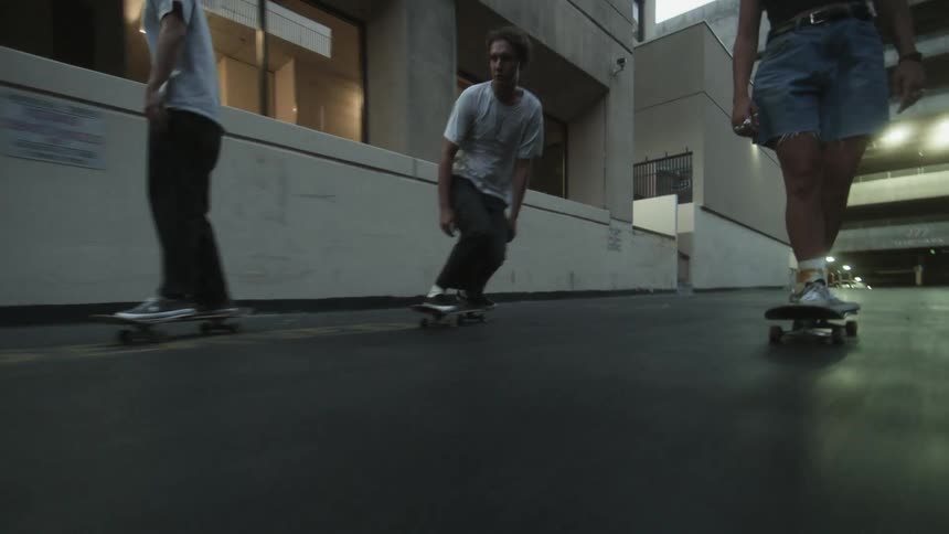 A group of skateboarders skate down an alleyway between buildings during the day