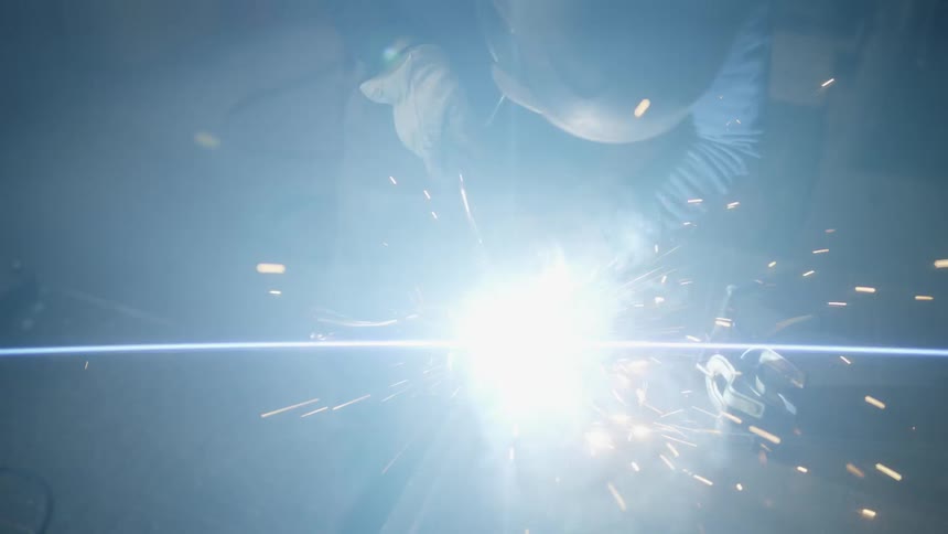 A welder makes a weld on a long metal rod which generates bright sparks