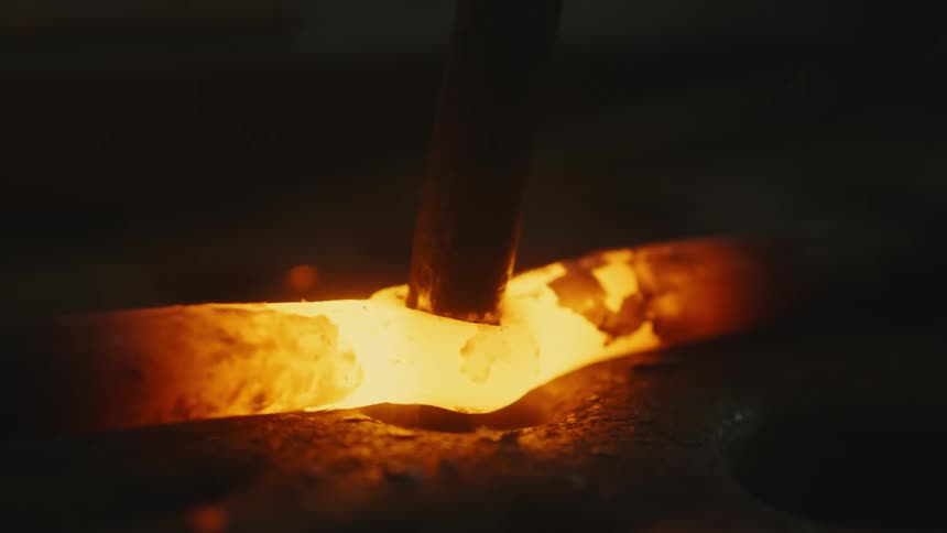 A chisel is used to shape a glowing hot piece of metal rod