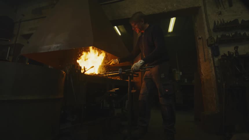 A man using tools to to manipulate fire in a pit