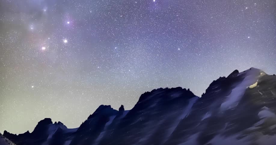 Time lapse of the stars on the night sky moving over the snow covered mountains