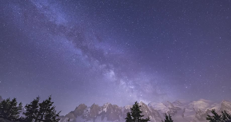 A view looking up at the starry sky as it gets deep purple overlooking mountain peaks