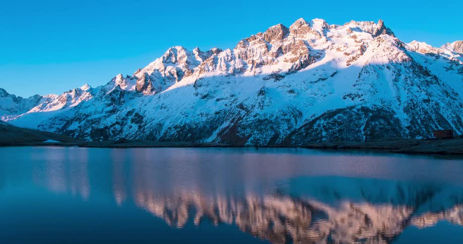 Snow covered mountain ranges reflecting off a body of water at the bottom of the mountain