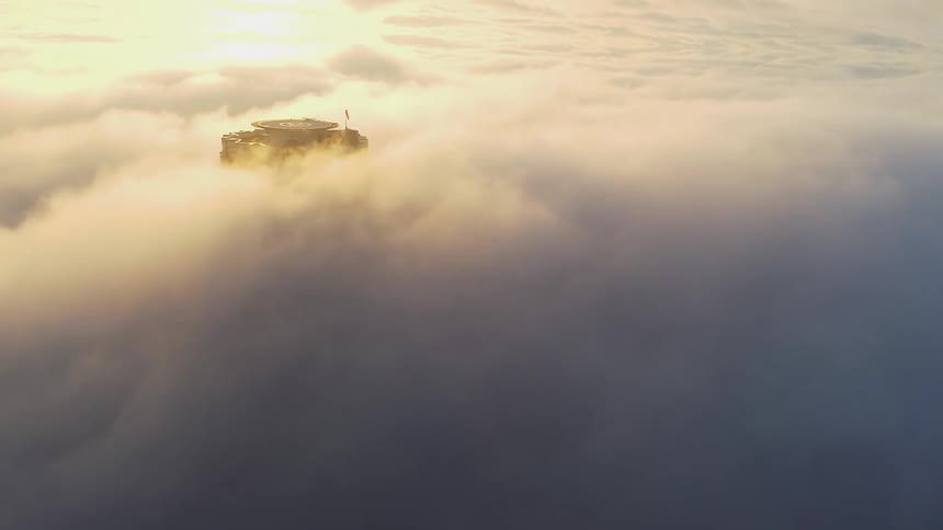 Sun shines on thick fog flowing around tower