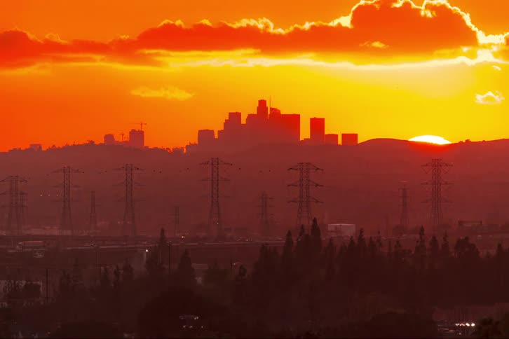 The sun sets behind the silhouettes of skyscrapers looming in the distance