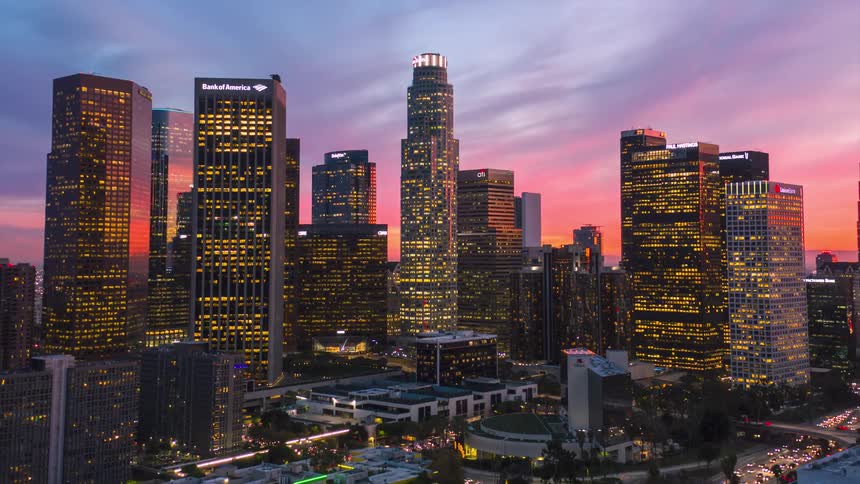 Lights on towers and skyscrapers glow in a busy metropolitan city as traffic fills the streets and colorful clouds move across the sky