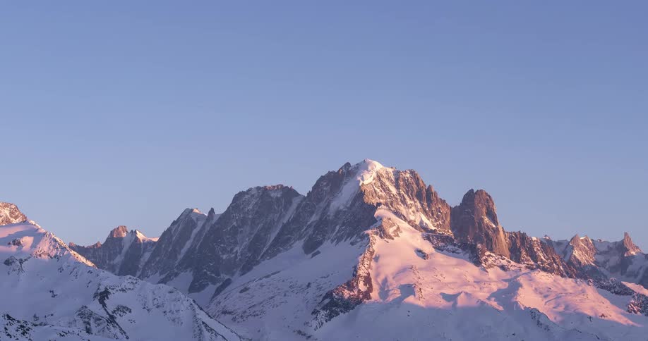 Sunlight moves across snow covered mountains turning red as sun sets
