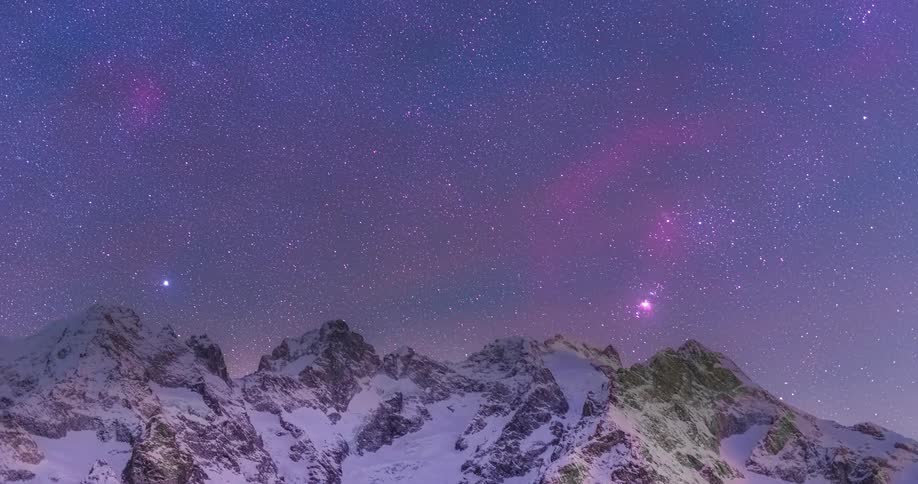 Stars in the night sky move over mountains and glow among pink clouds